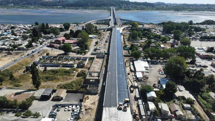 El Ministerio de Obras Públicas (MOP) de la Región del Biobío, por medio de la dirección de Vialidad, informó acerca de los avances en el proceso de asfaltado de la superestructura, también de la instalación de barreras laterales de hormigón, entre otros aspectos. Así lo confirmó el seremi de Obras Públicas, Hugo Cautivo, quien expresó que “estamos ya entrando en una etapa final de lo que es el viaducto Chacabuco, con los trabajos de asfaltado de la superficie de rodado, que en poco tiempo más permitirá transitar por este lugar”. “En este minuto estamos terminando lo que son las pavimentaciones, lo que son los muros aledaños. Esperamos que durante los primeros días de marzo esto ya esté terminado en lo que es el área de trabajo del viaducto Chacabuco”, dijo Cautivo. La obra, que ya cuenta con la instalación completa de sus vigas estructurales, tiene como prioridad enfocarse en los acabados finales, como las aceras de hormigón y ciclovías. Por otro lado, en el nuevo anfiteatro de San Pedro de la Paz se progresa con las gradas, en un espacio que permitirá la realización de actividades culturales, recreativas, y que va a implicar de alguna forma un aporte al desarrollo”, destacó la autoridad del MOP. Respecto de los plazos, Cautivo adelantó que “tuvimos que realizar una modificación del convenio de este contrato por el cambio de normativa en materia de iluminación, lo que también significó un cambio de diseño. Ya con esas autorizaciones vamos a empezar recién con la ejecución de obra de todo lo que es el proyecto de iluminación a partir de marzo de este año y por lo mismo la fecha de término, desde el punto de vista contractual se proyecta para junio de este año”. Se estima que el viaducto esté finalizado en junio del 2026, con el objetivo de aportar notoriamente a la reducción de tiempos de viaje y la descongestión vial en la comuna de San Pedro de la Paz y la conexión con Concepción.